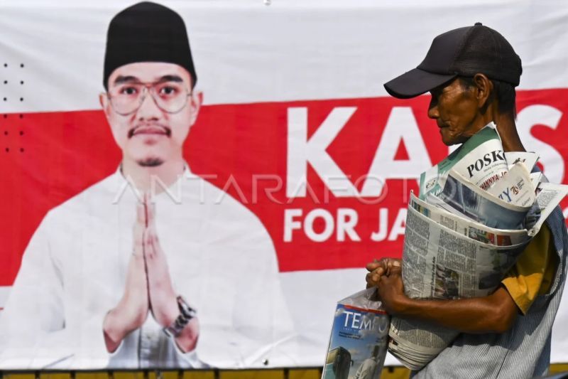 Penjual koran melintas di depan alat peraga sosialisasi bergambar Ketua Umum PSI Kaesang Pangarep