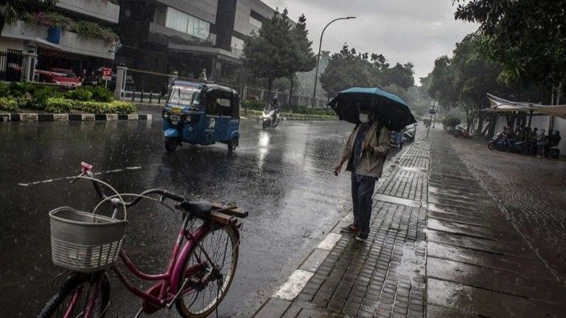 Arsip warga berjalan menggunakan payung saat hujan di kawasan Kelurahan Gambir