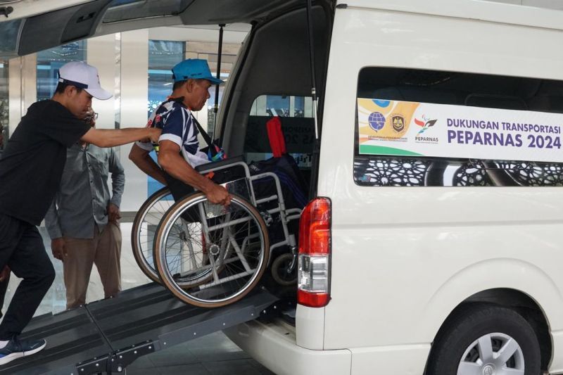 Seorang atlet menggunakan kursi roda sedang didorong memasuki kendaraan