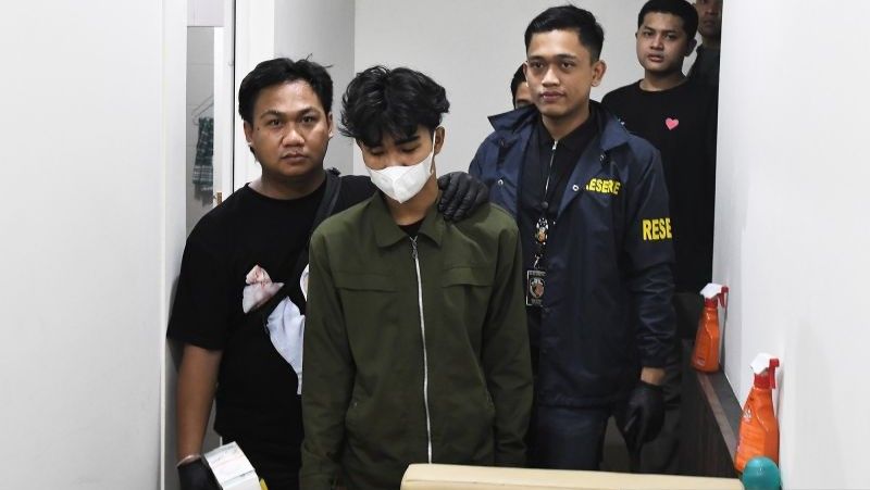 Personel Ditreskrimum Polda Metro Jaya menggiring seorang tersangka judi online di kantor Kemkomdigi
