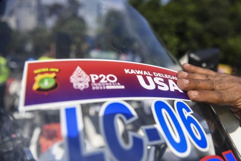 personel kepolisian menempelkan stiker pengawalan delegasi di kendaraan