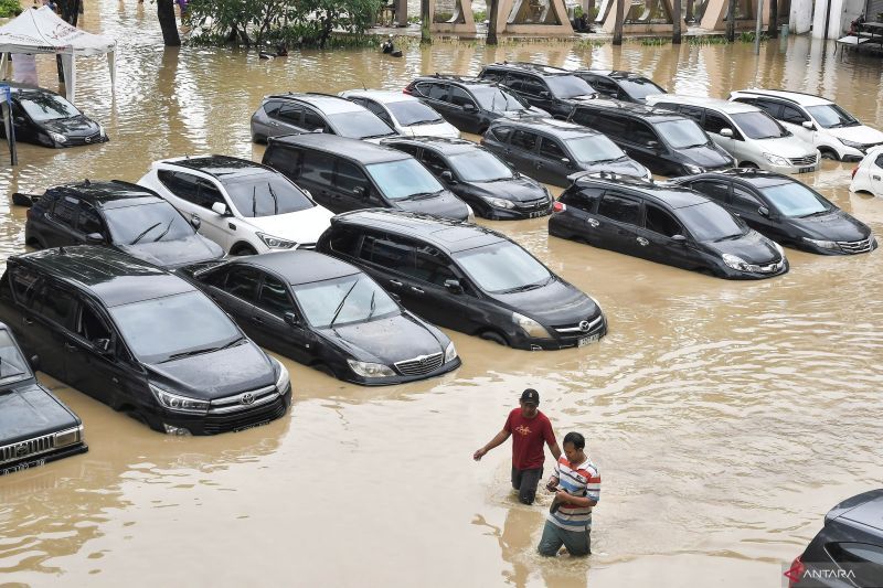 Warga melintas disamping mobil yang terendam banjir di pertokoan Galaxy,
