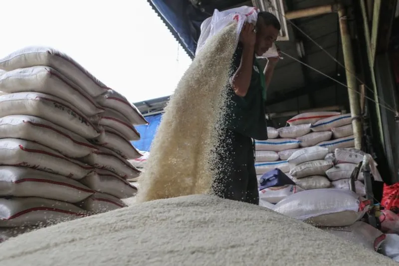 Pekerja menuangkan karung beras di Pasar Induk Beras Cipinang