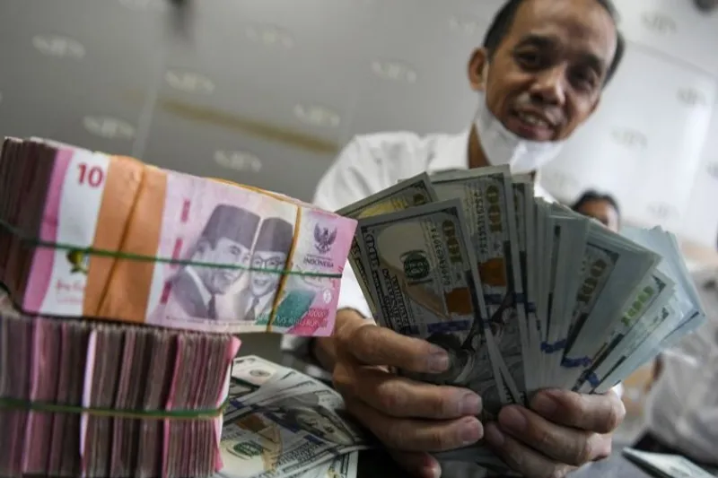Petugas menjunjukkan uang pecahan dolar AS dan rupiah