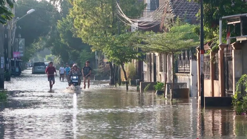 Warga saat melintasi jalan yang tergenang air akibat hujan lebat di Kota Mataram NTB