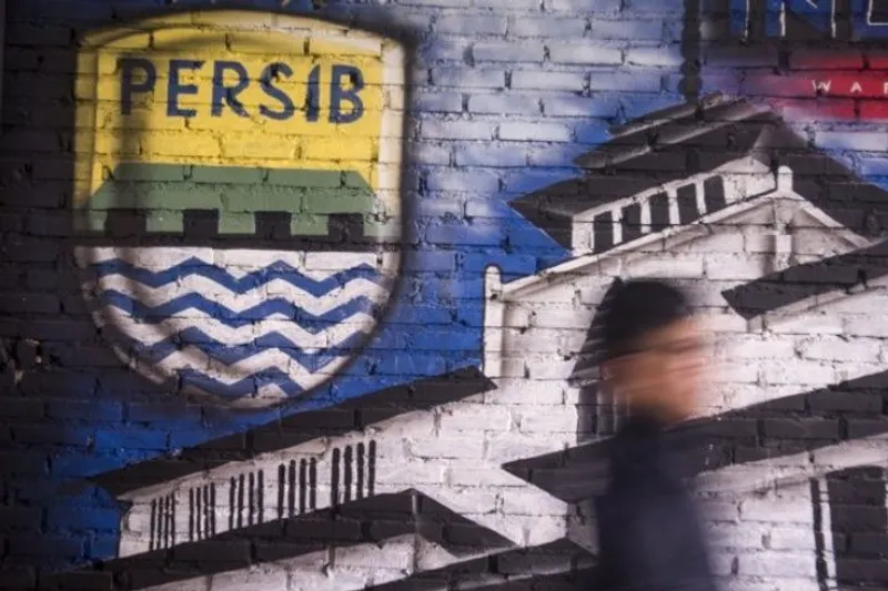 Seorang bobotoh alias pendukung Persib berjalan di depan mural Persib
