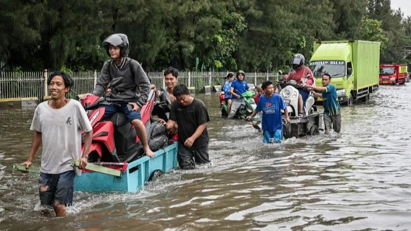 Pengendara sepeda motor menaiki gerobak untuk menerobos banjir di ruas Jalan Jembatan Tiga Raya