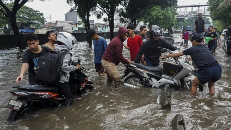 Warga membantu pengendara sepeda motor yang mogok saat menerobos banjir di Jakarta